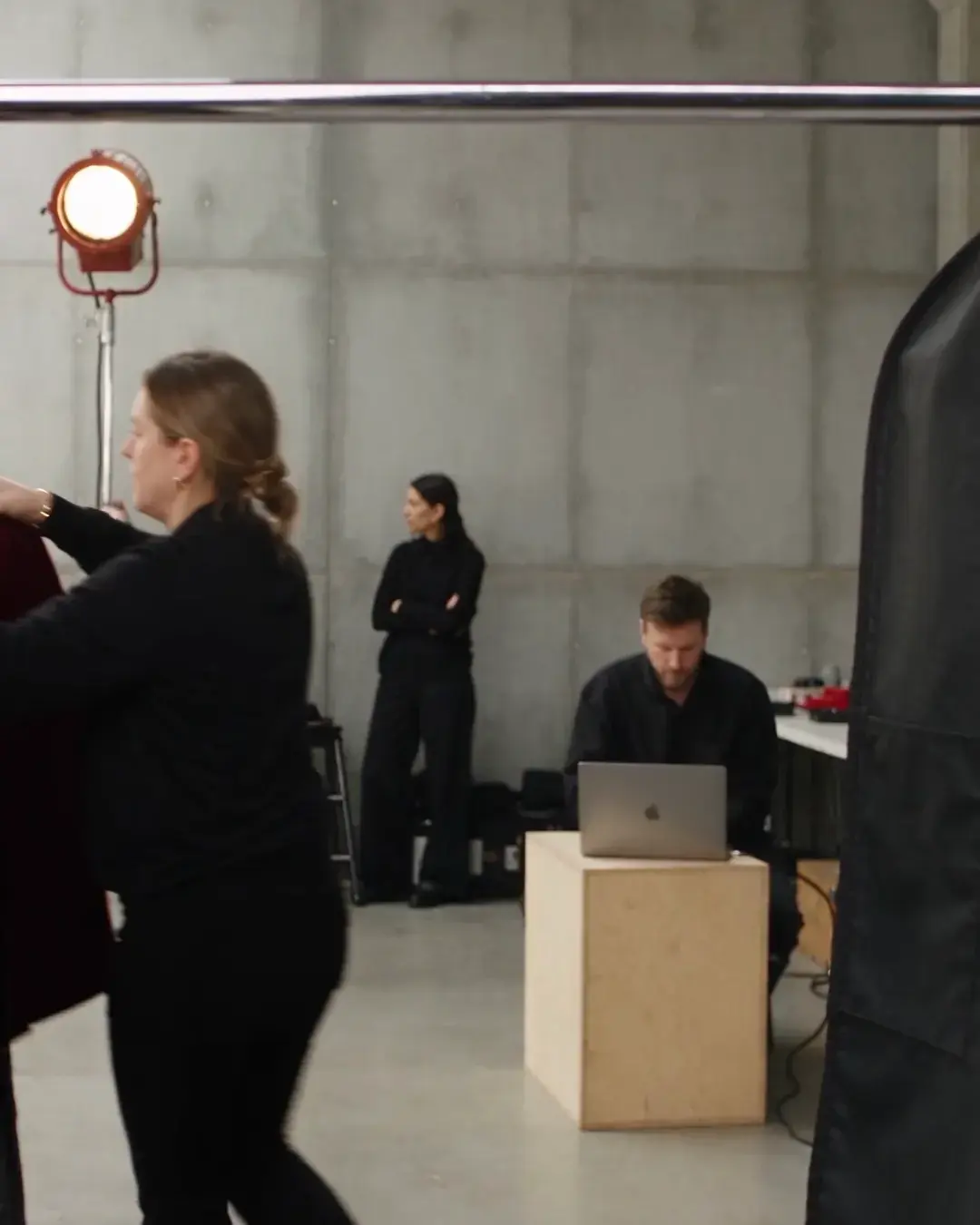 Crew at work on set: a laptop on a crate, a light stand, people in black