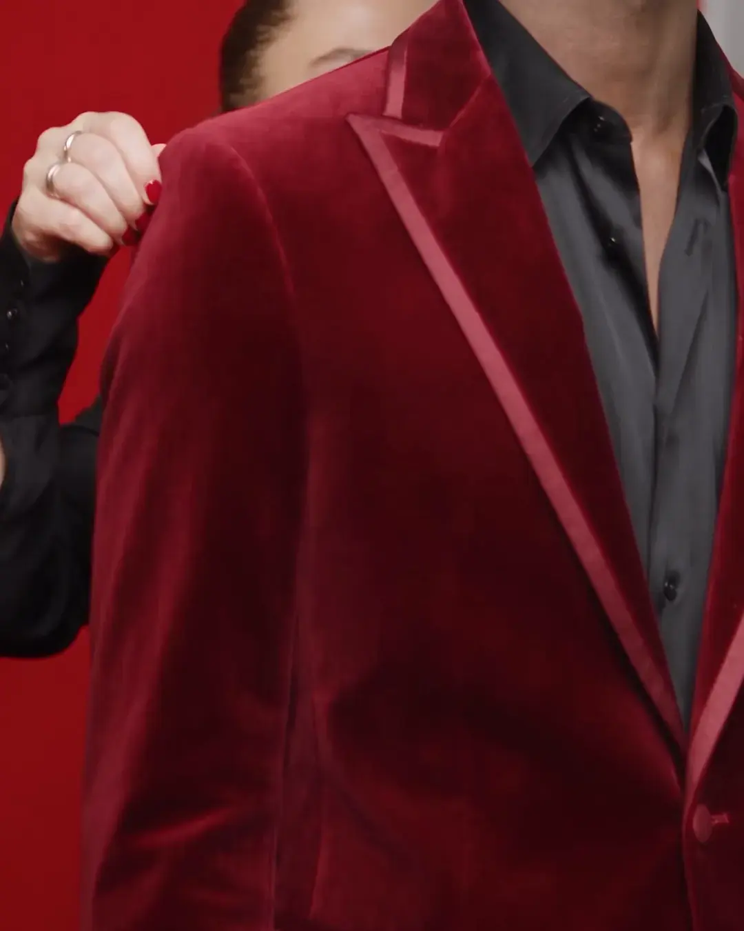 Two hands straightening the lapel of a burgundy velvet jacket, close in