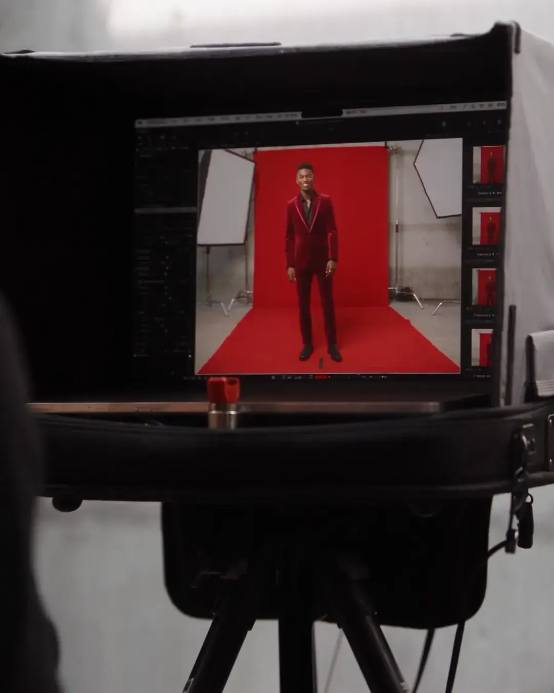 A monitor on the camera rig showing the framed shot, the model small and lit on red