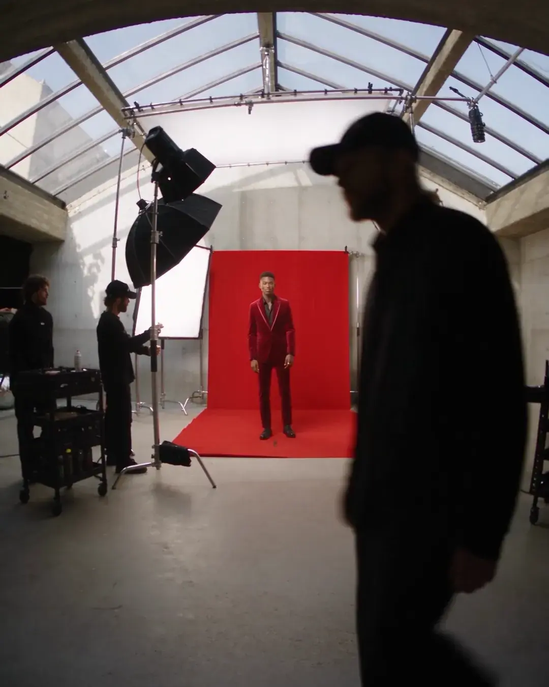 A studio hall: two big lights, a red paper sweep, a crew member crossing the frame
