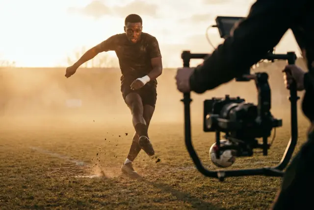 A cinema camera tracking a footballer mid-kick on a hazy pitch at golden hour